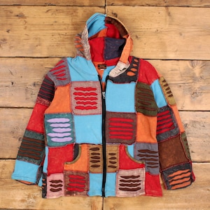 Op de afbeelding: Een kleurrijke patchwork hoodie met een lange ritssluiting. De jas heeft een verscheidenheid aan kleuren, waaronder rood, oranje, blauw en bruin, met een mix van rechthoekige en vierkante patches. De hoodie heeft een capuchon en twee voorzakken.