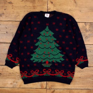 May include: Navy blue Christmas jumper with a green Christmas tree design, red baubles, and red snowflake accents. The jumper also features red bows and gift boxes along the bottom. A festive holiday garment.