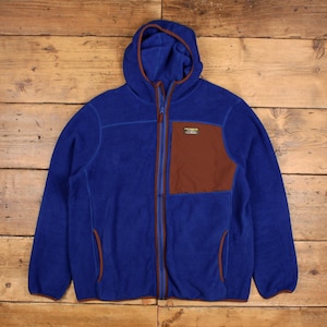 Może przedstawiać: Niebieska kurtka polarowa z kapturem i brązową kieszenią na piersi. Kurtka ma pełny zamek błyskawiczny i małą naszywkę z logo na piersi. Wykonana z miękkiego, ciepłego materiału, idealna do aktywności na świeżym powietrzu.