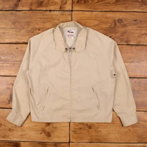 Puede incluir: Chaqueta beige con cremallera, cuello y dos bolsillos delanteros. La chaqueta tiene cierre de cremallera completo y mangas largas. El logotipo de la marca es visible en el cuello. La chaqueta es de material ligero.