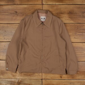 May include: A tan jacket with a full zipper closure, two front pockets, and a collared neckline. The jacket has a button closure on the cuffs and the brand name "Mac-Mor" is visible on a small tag near the collar.
