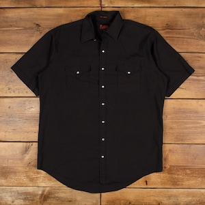 Könnte beinhalten: Schwarzes kurzärmeliges Hemd mit Knopfleiste und zwei Brusttaschen. Das Hemd hat einen klassischen Western-Stil mit spitzem Kragen und Perlmutt-Druckknöpfen. Das Hemd ist aus einem einfarbigen schwarzen Stoff gefertigt.