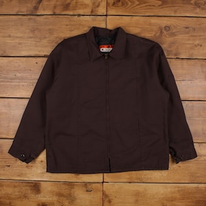May include: A dark brown zip-up jacket featuring a classic collar, long sleeves with buttoned cuffs, and vertical seam detailing on the front. The interior neck label displays the text X and additional illegible white text on a red background.