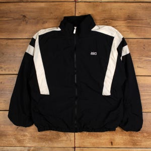 Könnte beinhalten: Schwarze Jacke mit Reißverschluss und weißen Schulter- und Ärmelakzenten. Die Jacke hat einen hohen Kragen und das "asics"-Logo auf der Brust. Hergestellt aus leichtem Material, geeignet für Sport oder Freizeit.