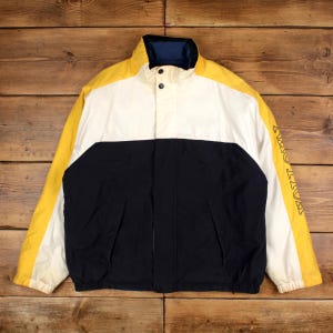 May include: A vintage jacket in yellow, white, and navy blue. The jacket has a stand-up collar with a blue interior, two front pockets, and the word "HUTTON" printed in yellow on the left sleeve.