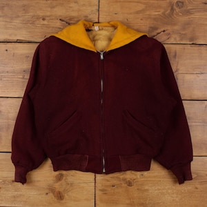 Peut inclure: Veste zippée bordeaux avec capuche jaune et intérieur duveteux. La veste a deux poches avant et des poignets et un ourlet côtelés. La veste est faite d'une matière épaisse et chaude, idéale pour les temps frais.