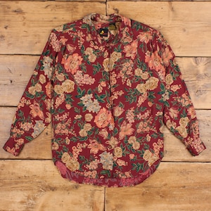 May include: A long-sleeved button-up shirt with a floral print in shades of red, pink, green, and white. The shirt has a collar and a button-up front.