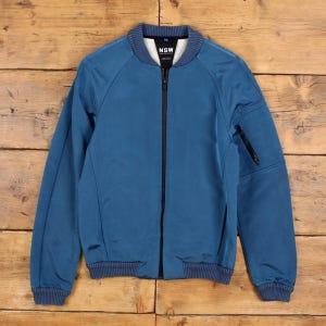 May include: Blue bomber jacket with a black zip and ribbed cuffs and hem. The jacket features a small pocket on the left sleeve and the letters "NSW" on the collar. Made from a smooth, lightweight material.