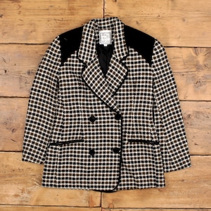 Może przedstawiać: Dwurzędowa marynarka w pepitkę w kolorze czarnym, białym i oliwkowym, z czarnymi aksamitnymi wstawkami na ramionach i wykończeniami. Marynarka ma dwa rzędy czarnych guzików, a na metce widnieje napis "WALDO WEAR".