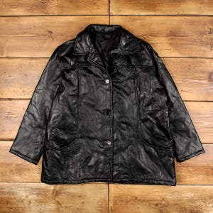 May include: A black leather jacket featuring a classic collar, long sleeves, and a front button closure with three visible buttons. The garment is constructed from multiple stitched panels of black leather, creating a textured surface.