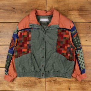 Può includere: Giacca vintage con design patchwork. La giacca ha un corpo verde, colletto e maniche color pesca. I pannelli anteriori e le maniche presentano motivi geometrici colorati in rosso, arancione e blu. La giacca ha una chiusura con bottoni e due tasche.