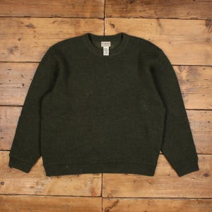 Peut inclure: Un pull à col rond vert olive foncé avec des manches longues, un col côtelé et des poignets côtelés. Le vêtement comporte une étiquette de marque rectangulaire blanche cousue à l'intérieur du col avec le texte L.L.Bean visible.