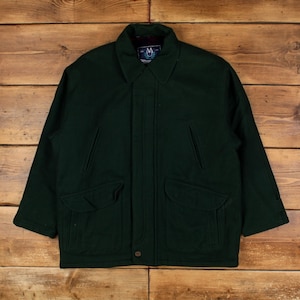 May include: A dark forest green wool-blend jacket featuring a pointed collar, a front button placket, two large flap pockets at the waist, and two vertical slit pockets on the chest. The interior label displays the letters M and A in a crest.