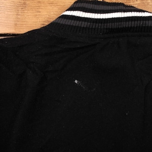 Puede incluir: Primer plano de un cuello de chaqueta negro con un diseño a rayas en blanco, gris y negro. La chaqueta parece estar hecha de una tela suave y texturizada. El cuello es acanalado.