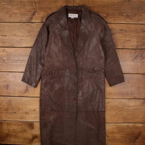 May include: A long, brown leather coat with a button-up front, lapel collar, and shoulder epaulets. The coat has a tailored fit and a knee-length hemline. The coat is made of a soft, supple leather material.