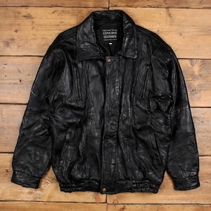 Può includere: Giacca in pelle nera con collo, due tasche frontali e chiusura con bottoni. La giacca ha orlo e polsini a coste. L'etichetta recita "Genuine Leather".