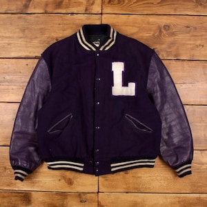 May include: A purple varsity jacket with leather sleeves. The jacket has a large white letter "L" on the chest and striped detailing on the collar, cuffs, and hem. The jacket is buttoned up and has two front pockets.