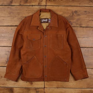May include: A brown leather jacket with a collared neckline and four front pockets. The jacket has a button-up closure and the brand name "Schott" is visible on the label.