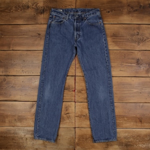 Könnte beinhalten: Blaue Jeans aus Denim mit Knopfleiste, Fünf-Taschen-Design und geradem Bein. Die Jeans hat eine mittelblaue Waschung mit dezenten Ausbleichungen und Gebrauchsspuren. Das Kleidungsstück liegt flach auf einer Holzoberfläche.