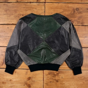 May include: A vintage patchwork leather jacket in black, grey, and green. The jacket has a geometric design with a black ribbed hem and cuffs. The sleeves are long and the neckline is round.