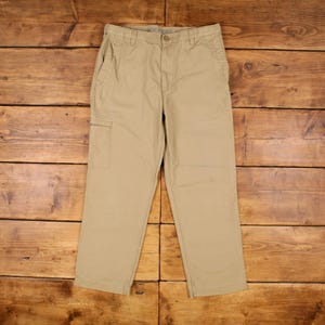 May include: Khaki-coloured Dockers trousers with a button closure and side pocket. The trousers are made of a durable fabric and have a classic, straight-leg fit. The trousers are displayed on a wooden surface.