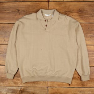 May include: A tan long-sleeved collared shirt with a three-button placket. The shirt has a textured pattern and a ribbed hem and cuffs. The brand "ORVIS" is visible on the collar.