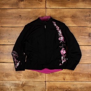 Puede incluir: Chaqueta negra con un diseño floral rosa en el lado derecho y la palabra "Rockstar" bordada en la manga izquierda.
