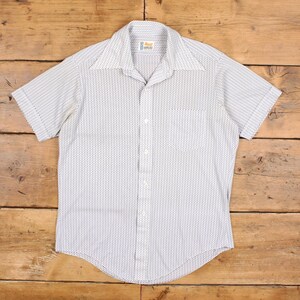 May include: White short-sleeved shirt with a small, repeating pattern of dark dots. The shirt features a classic collar, a chest pocket, and a button-down front. The shirt is made of a lightweight fabric.