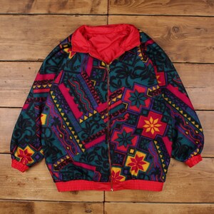 May include: A colorful zip-up jacket with a geometric pattern in teal, fuchsia, purple, and yellow. The jacket has a red collar, cuffs, and lining. The jacket is made of a soft material.