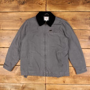 May include: A grey zip-up jacket featuring a black corduroy collar, long sleeves, and two front pockets. The garment includes a Wrangler brand label on the interior neck and a small rectangular logo patch on the upper left chest area.