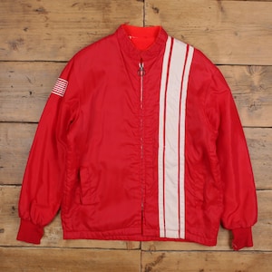 May include: A red jacket with a white stripe design down the front. The jacket has a stand-up collar, a zipper closure, and red cuffs. An American flag patch is on the left sleeve. The jacket is likely vintage or retro.