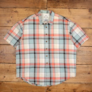 May include: Short-sleeved plaid shirt in a pastel colour palette of light blue, peach, cream, and black. The shirt has a button-down front, a collar, and a chest pocket. The brand name is visible on the collar.