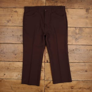 May include: A pair of solid dark brown trousers featuring a structured waistband with belt loops, a central button closure, and two front pockets. The trousers have a straight-leg cut with a visible vertical crease running down the centre of each leg.