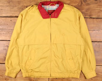 May include: A yellow jacket with a red collar and a full-length zipper. The jacket has two front pockets and a small embroidered design on the chest. The collar has a plaid lining.