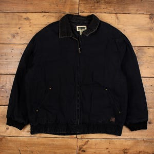 Peut inclure: Veste de travail noire avec un col en velours côtelé et une fermeture éclair intégrale. La veste a deux poches avant et un ourlet et des poignets côtelés. L'étiquette du col indique "SAFE OAK".