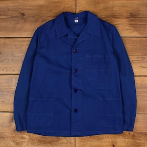May include: A cobalt blue work jacket with a button-up front, a notched collar, and three front pockets. The jacket has long sleeves and is made of a durable fabric. The jacket is laid flat on a wooden surface.