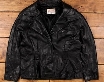 May include: A black leather jacket with a notched collar and button closure. The jacket has a classic design with a small pocket on the chest and decorative stitching. The label reads "PELLE STUDIO".