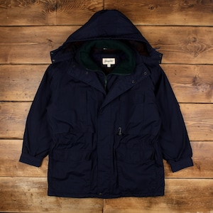 Op de afbeelding: Een marineblauwe jas met capuchon en een groene en bruine binnenvoering. De jas heeft een ritssluiting, meerdere zakken en een taille met trekkoord. De merknaam "Johnston" is zichtbaar.