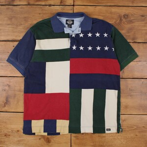 Könnte beinhalten: Ein kurzärmeliges Poloshirt mit Patchwork-Design. Das Shirt hat eine Mischung aus Farben, darunter Marineblau, Rot, Weiß, Grün und Beige. Die rechte Seite hat ein marineblaues Feld mit weißen Sternen und einem roten Streifen.