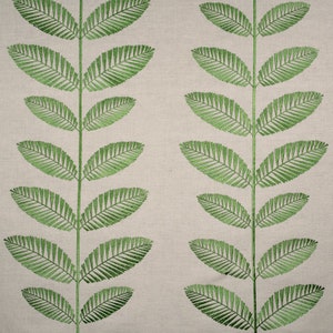 May include: A beige fabric with a repeating pattern of green embroidered leaves. The leaves are stylized and resemble a fern.