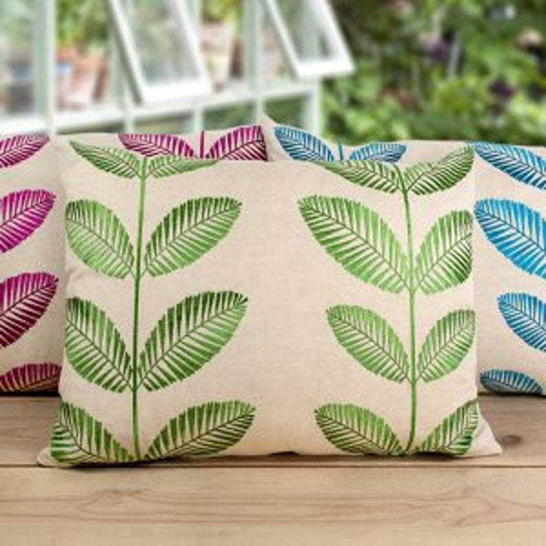 May include: Three decorative throw pillows with a leafy green pattern on a natural linen fabric. The pillows are arranged in a row on a wooden surface.