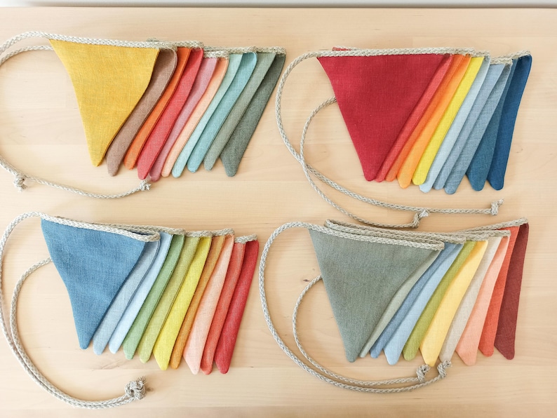 May include: Four sets of triangular fabric bunting flags arranged in groups. Each set features a variety of solid colors including yellow, red, blue, green, and orange, all attached to a thick, braided beige rope for hanging and display.