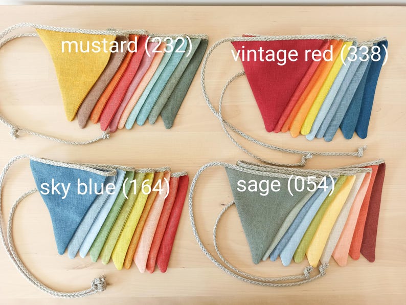 May include: Four sets of triangular fabric bunting flags attached to a braided rope. Each set features a gradient of colors, labeled as mustard (232), vintage red (338), sky blue (164), and sage (054), showcasing various textile hues.