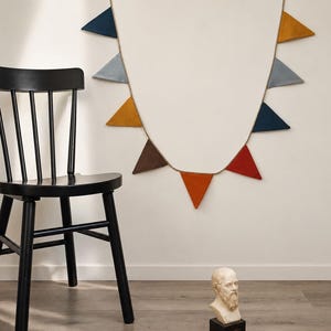 Puede incluir: Una silla de madera negra con respaldo de husillo se encuentra junto a un espejo de pared decorado con banderas triangulares de colores. Un pequeño busto de un hombre barbudo descansa sobre una base negra en el suelo.