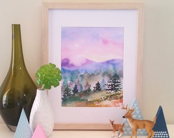 Può includere: Dipinto ad acquerello incorniciato di un paesaggio montano viola e rosa con alberi verdi. Il dipinto è su uno sfondo bianco ed è circondato da una cornice in legno chiaro. Ci sono due piccole statuine di cervi di legno in primo piano.