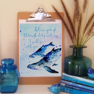 May include: A watercolour print with a quote about going through deep waters. The quote reads "When you go through deep waters I will be with you". The print features three blue whales swimming in a blue and white watercolour background.
