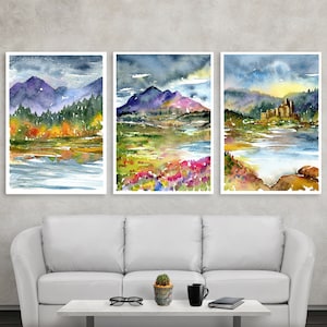 May include: Three watercolour paintings of landscapes with mountains, lakes, and forests. The paintings are framed and hung on a wall above a white sofa.