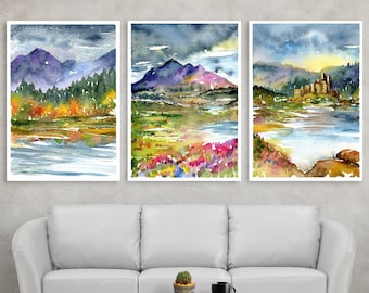 Può includere: Tre acquerelli di paesaggi con montagne, laghi e foreste. I dipinti sono incorniciati e appesi a una parete sopra un divano bianco.