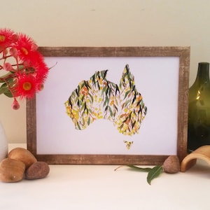May include: A framed print of a watercolour illustration of the outline of Australia filled with yellow and green flowers. The print is on a white background and is framed in a natural wood frame.