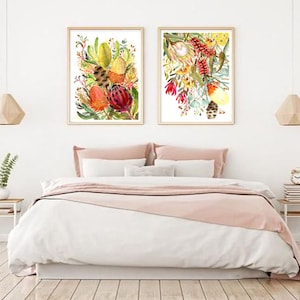 Puede incluir: Dos pinturas de acuarela enmarcadas de flores nativas australianas coloridas, que incluyen tonos rojos, amarillos y verdes, que se muestran en una pared blanca sobre una cama con ropa de cama rosa.